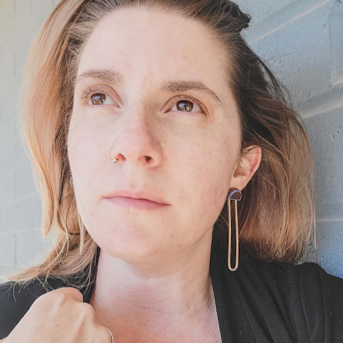 Woman wearing stud earrings made from painted wood and brass chains.