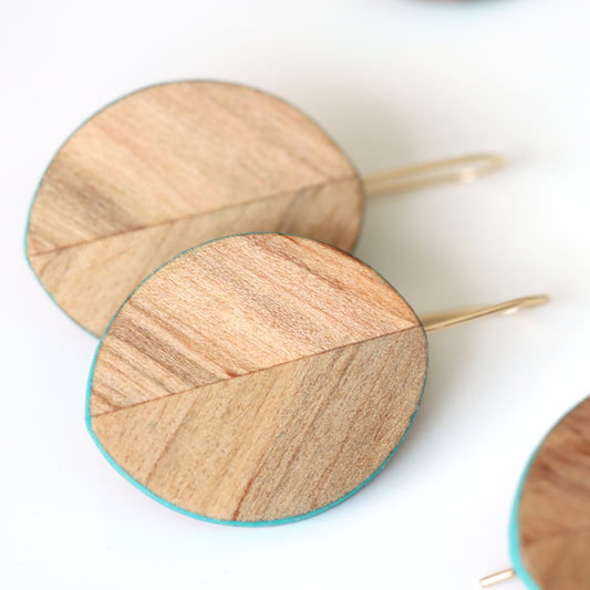 Close up of leaf shaped wood carved earrings with turquoise accents.