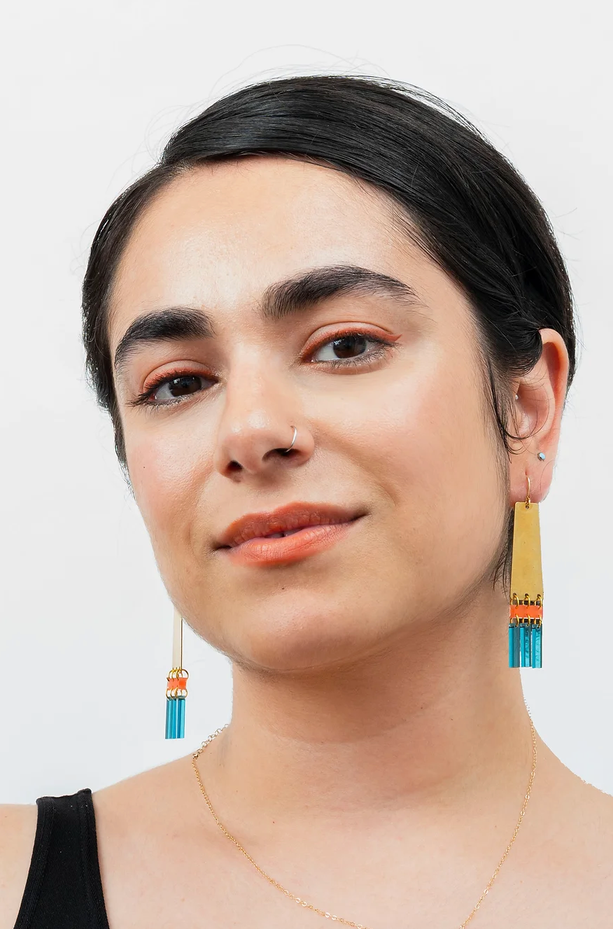 Woman wearing brass and colorful acrylic earrings with fringe.